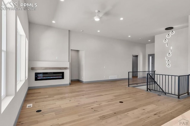 living area with recessed lighting, visible vents, a glass covered fireplace, light wood-type flooring, and baseboards