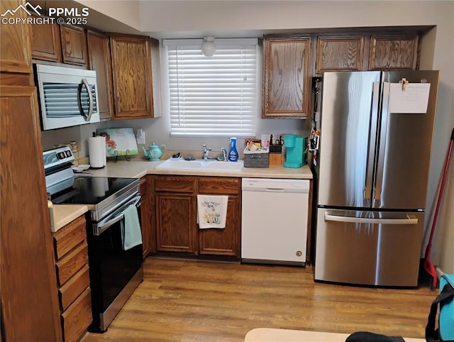 kitchen with appliances with stainless steel finishes, light wood-type flooring, light countertops, and a sink