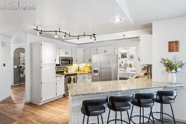 kitchen with arched walkways, a peninsula, appliances with stainless steel finishes, backsplash, and light wood finished floors