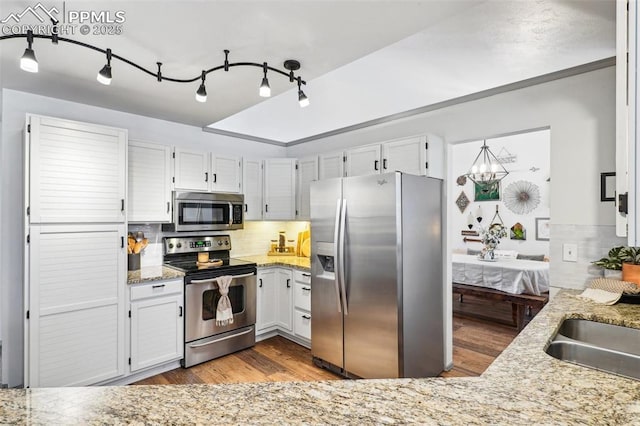 kitchen with light stone countertops, appliances with stainless steel finishes, decorative backsplash, and wood finished floors