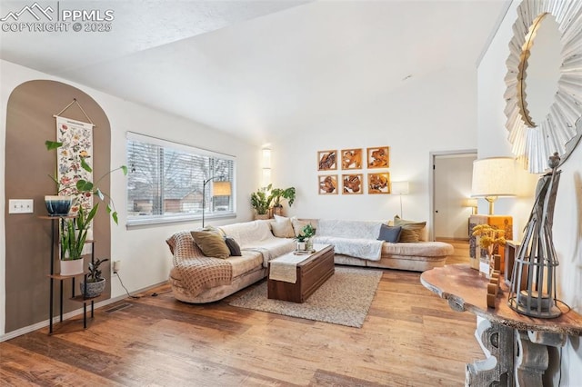 living area with vaulted ceiling, arched walkways, and light wood-style floors