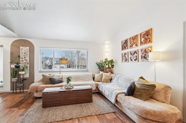 living area featuring lofted ceiling, arched walkways, and wood finished floors