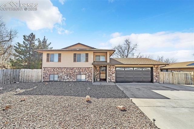 tri-level home featuring a garage, stone siding, fence, and driveway