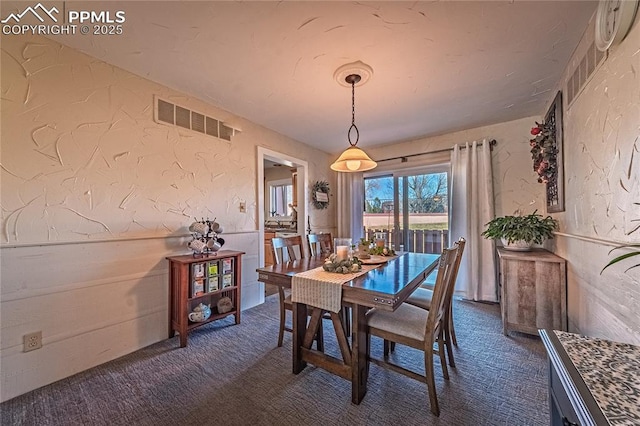 dining area featuring dark colored carpet, wainscoting, visible vents, and a textured wall