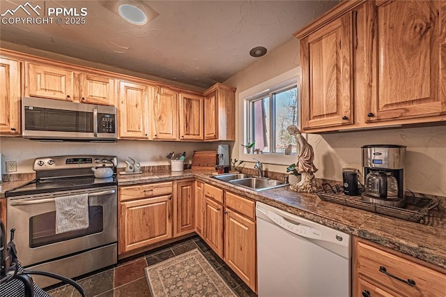 kitchen with stainless steel appliances, dark countertops, a sink, and stone tile floors