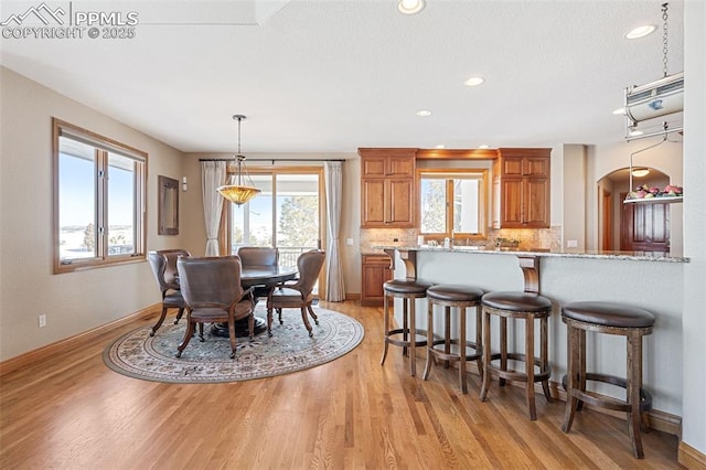 dining area featuring baseboards, light wood-type flooring, arched walkways, and recessed lighting