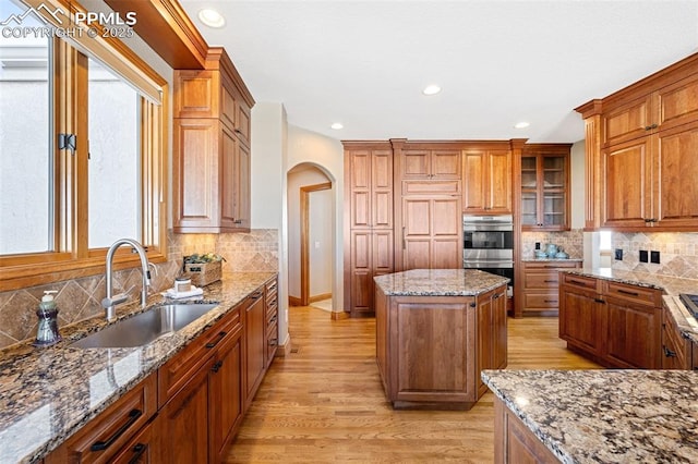 kitchen featuring arched walkways, light wood finished floors, double oven, a sink, and light stone countertops