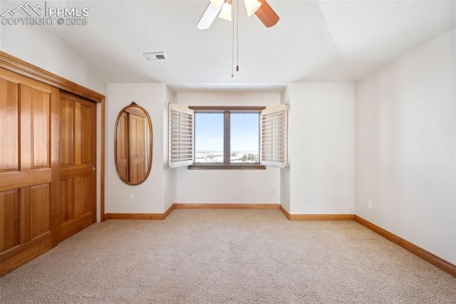 carpeted spare room with a ceiling fan, baseboards, and a textured ceiling