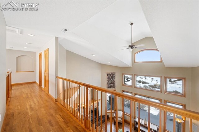 corridor featuring baseboards, visible vents, an upstairs landing, light wood-type flooring, and high vaulted ceiling