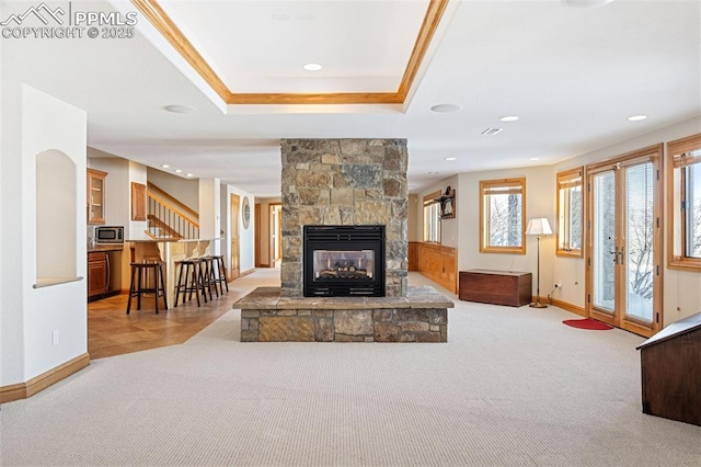 living area featuring light carpet, a stone fireplace, a raised ceiling, and baseboards