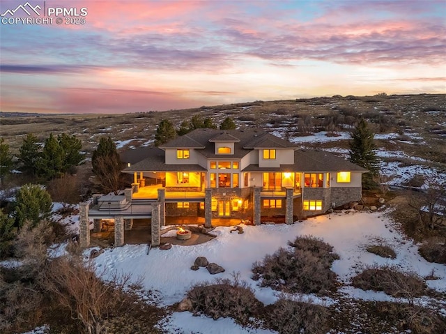 snow covered back of property with stone siding and a balcony