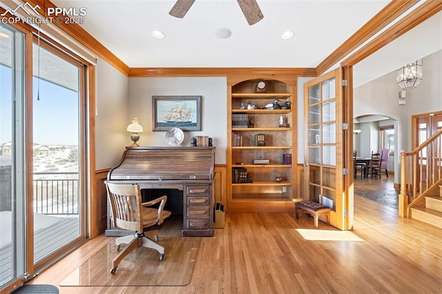 living area featuring built in features, arched walkways, crown molding, wood finished floors, and stairs