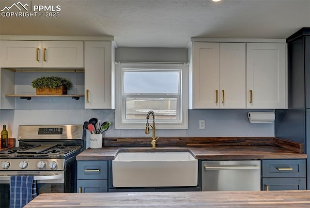 kitchen featuring stainless steel appliances, butcher block countertops, a sink, and white cabinets