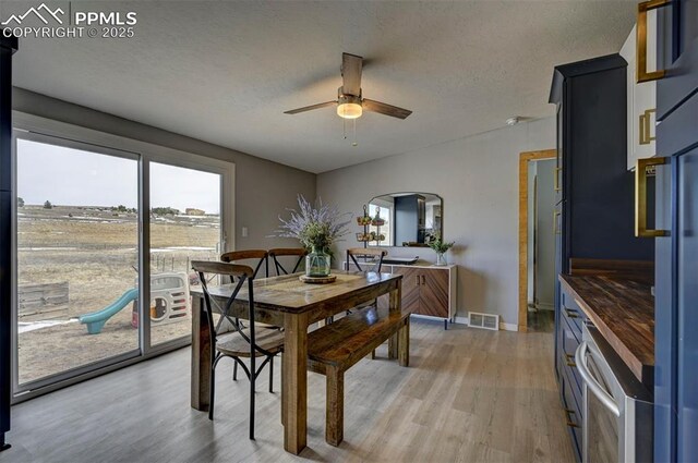 dining room with a textured ceiling, visible vents, baseboards, a ceiling fan, and light wood finished floors