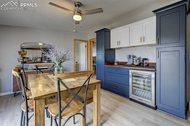 kitchen featuring white cabinets, wine cooler, blue cabinets, light wood-style floors, and wooden counters