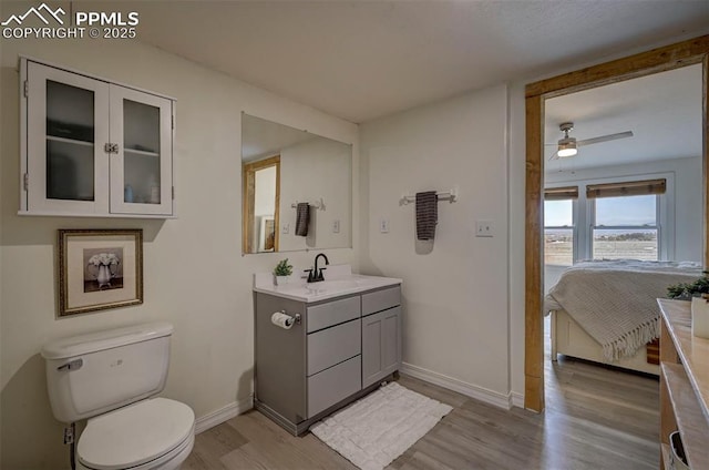 bathroom with toilet, ceiling fan, vanity, wood finished floors, and baseboards