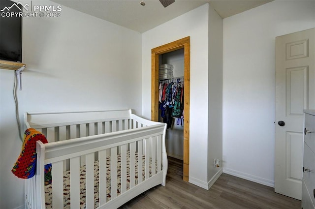 bedroom featuring a nursery area, baseboards, and wood finished floors