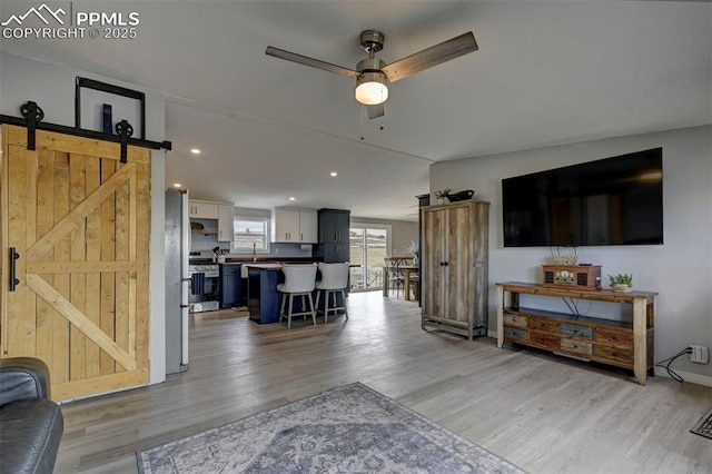 living room featuring light wood-type flooring, ceiling fan, recessed lighting, and a barn door