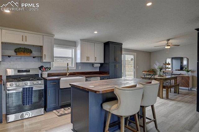 kitchen featuring butcher block counters, light wood-style flooring, stainless steel gas stove, a sink, and a kitchen bar