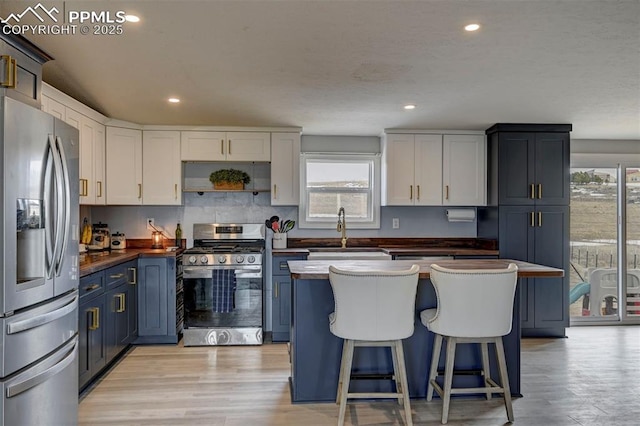 kitchen featuring blue cabinetry, appliances with stainless steel finishes, light wood-style floors, and a sink