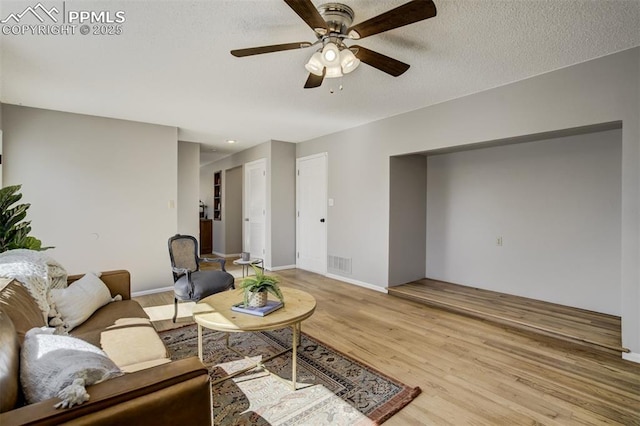 living room featuring light wood-style floors, visible vents, ceiling fan, and a textured ceiling