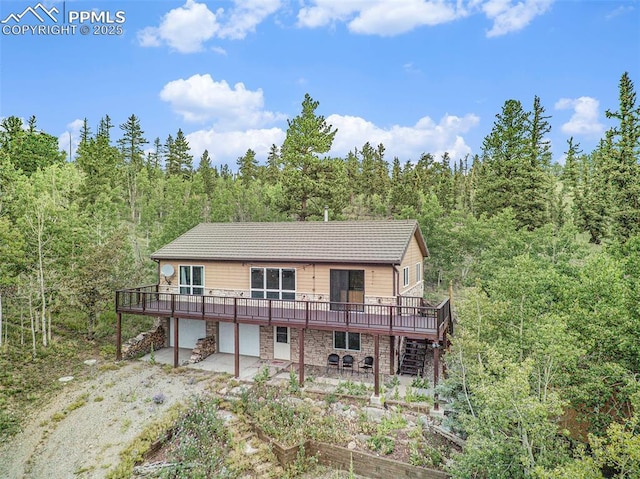 rear view of property featuring dirt driveway, stone siding, stairway, a vegetable garden, and a wooded view