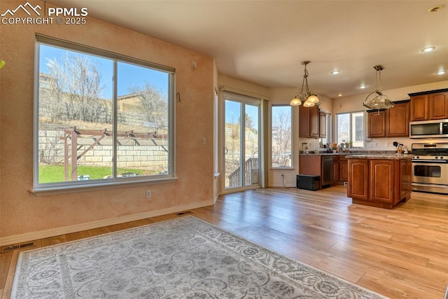 kitchen featuring visible vents, light wood-style flooring, appliances with stainless steel finishes, brown cabinets, and decorative light fixtures