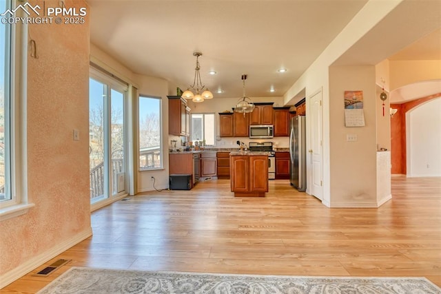 kitchen featuring visible vents, brown cabinets, a center island, stainless steel appliances, and light wood-style floors