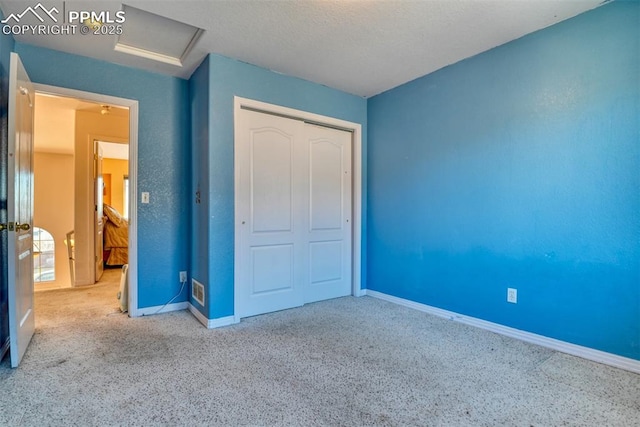 unfurnished bedroom featuring carpet, a closet, attic access, a textured ceiling, and baseboards