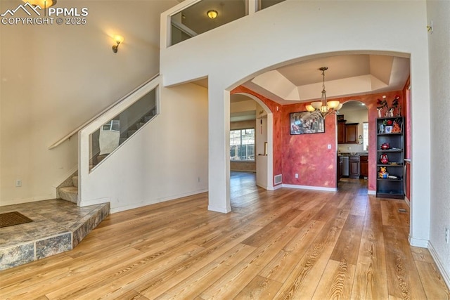 interior space featuring arched walkways, a tray ceiling, a notable chandelier, wood-type flooring, and stairway