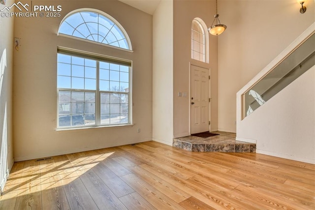 foyer entrance featuring visible vents, stairway, a towering ceiling, wood finished floors, and baseboards