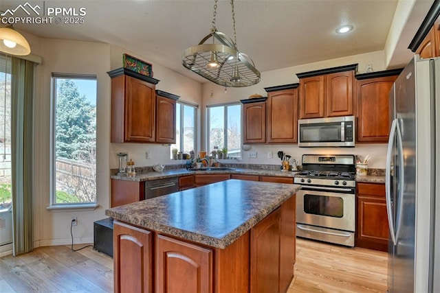 kitchen featuring stainless steel appliances, a sink, a kitchen island, light wood-style floors, and dark countertops