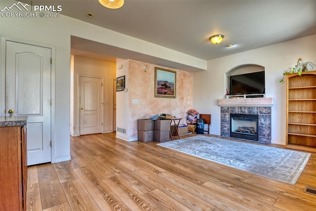 unfurnished living room with a tile fireplace, visible vents, light wood-style flooring, and baseboards