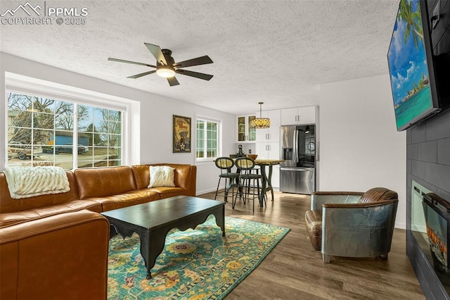 living room with a fireplace, dark wood-type flooring, a ceiling fan, a textured ceiling, and baseboards