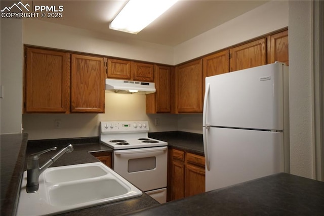 kitchen featuring white appliances, dark countertops, brown cabinets, under cabinet range hood, and a sink