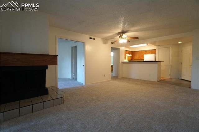 unfurnished living room featuring a textured ceiling, ceiling fan, a tile fireplace, light colored carpet, and visible vents