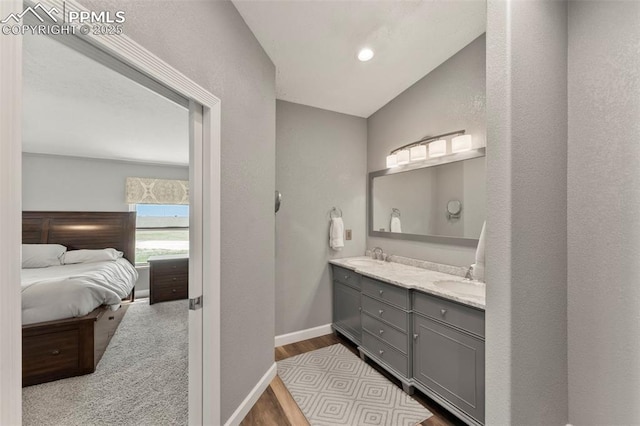 bathroom with double vanity, a sink, ensuite bath, wood finished floors, and baseboards