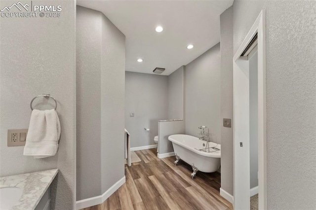 full bathroom with a freestanding tub, recessed lighting, wood finished floors, vanity, and baseboards