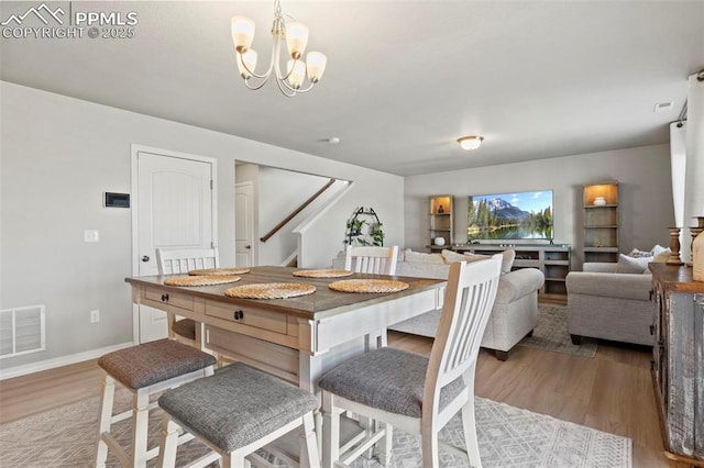 dining space featuring baseboards, visible vents, wood finished floors, an inviting chandelier, and stairs