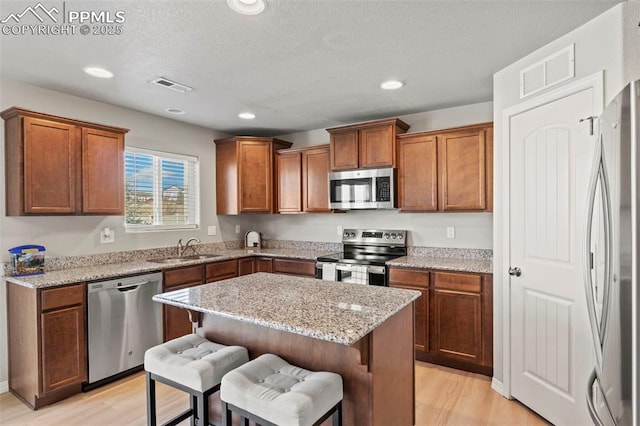 kitchen with stainless steel appliances, visible vents, a sink, and light wood finished floors