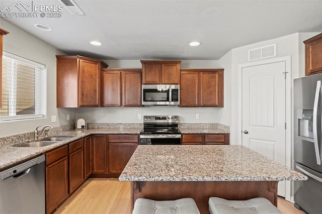 kitchen with light wood-style flooring, a sink, visible vents, a kitchen breakfast bar, and appliances with stainless steel finishes