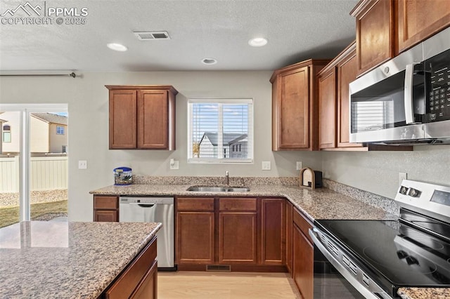 kitchen with brown cabinets, stainless steel appliances, visible vents, a sink, and light stone countertops