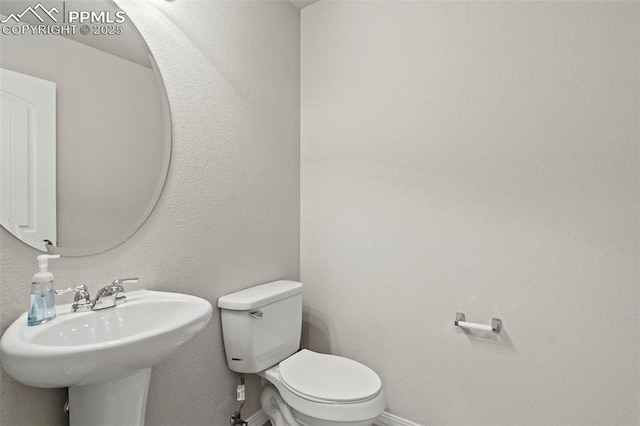 half bath featuring toilet, baseboards, and a sink