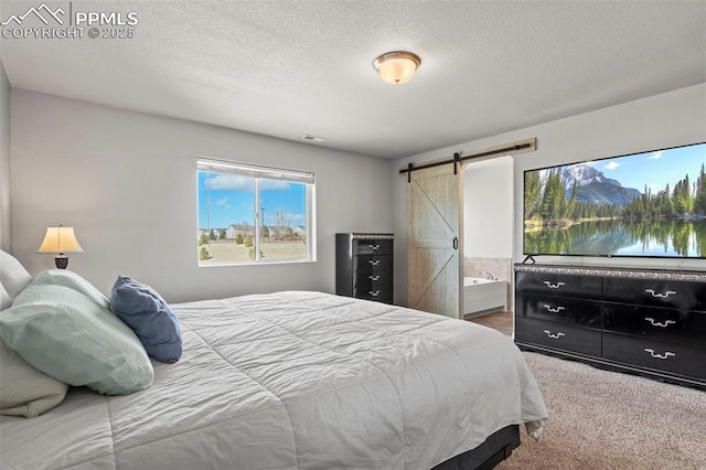 carpeted bedroom featuring a barn door, a textured ceiling, and ensuite bathroom