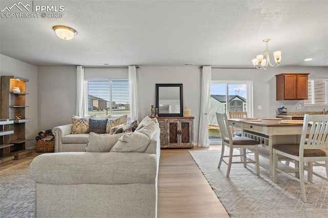 living area with a chandelier, a textured ceiling, light wood-type flooring, and visible vents