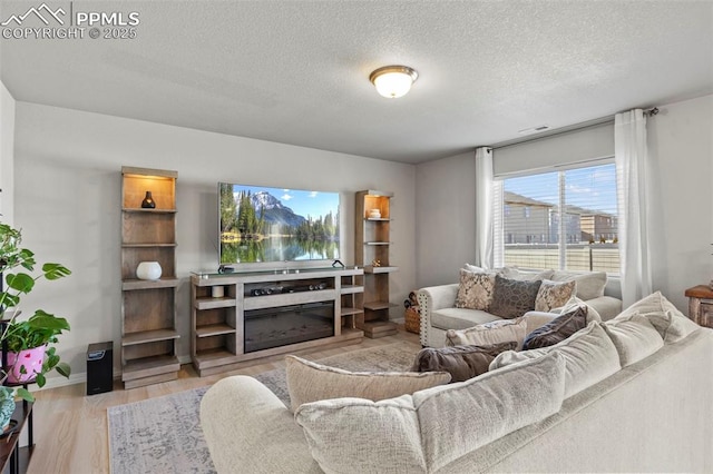 living room with a glass covered fireplace, visible vents, a textured ceiling, and wood finished floors