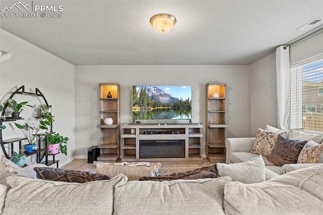 living room with visible vents, a glass covered fireplace, a textured ceiling, wood finished floors, and baseboards