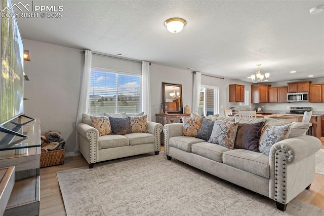 living room with light wood finished floors, a textured ceiling, and a notable chandelier