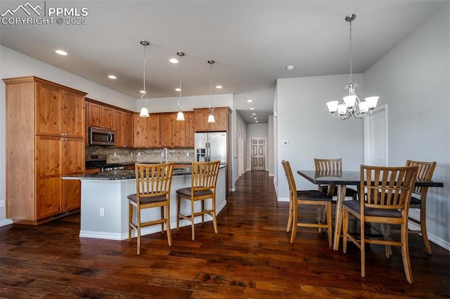 kitchen with brown cabinetry, dark wood-style floors, a breakfast bar area, stainless steel appliances, and backsplash