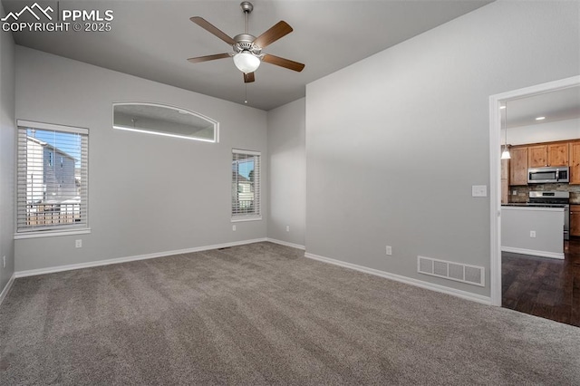 empty room with a ceiling fan, visible vents, dark carpet, and a wealth of natural light